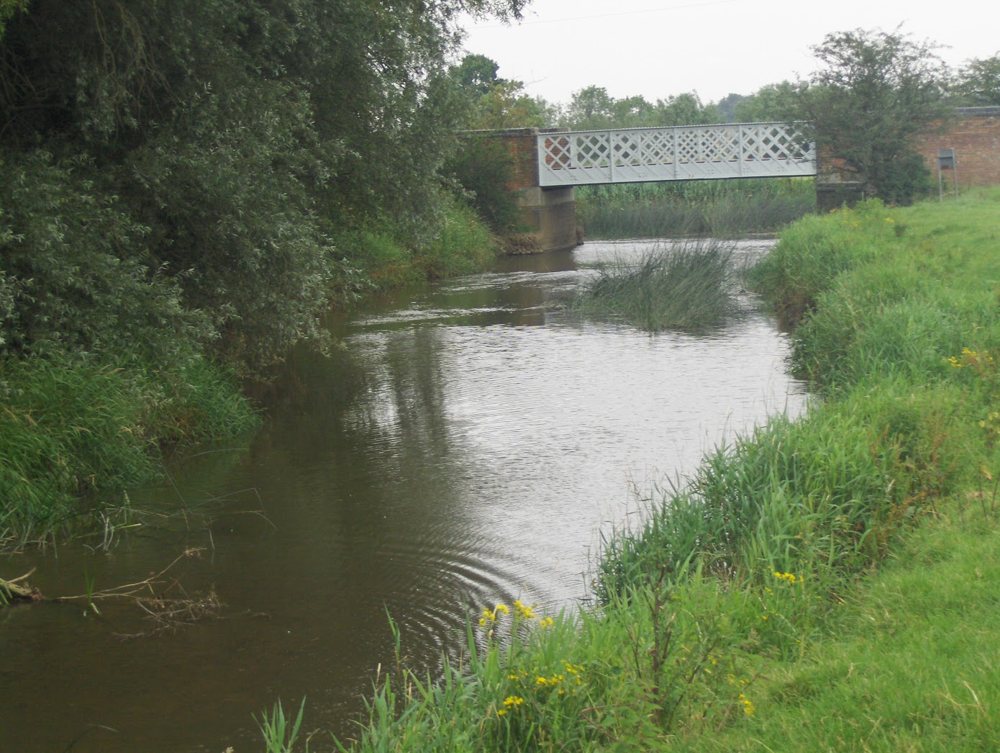 The River Cherwell flowing between grassy banks towards the iron lattice road bridge