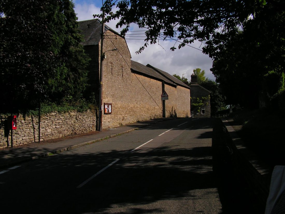 The long stone barns of Dovecote Farm beside the Heyford Road, with a red post box in the wall