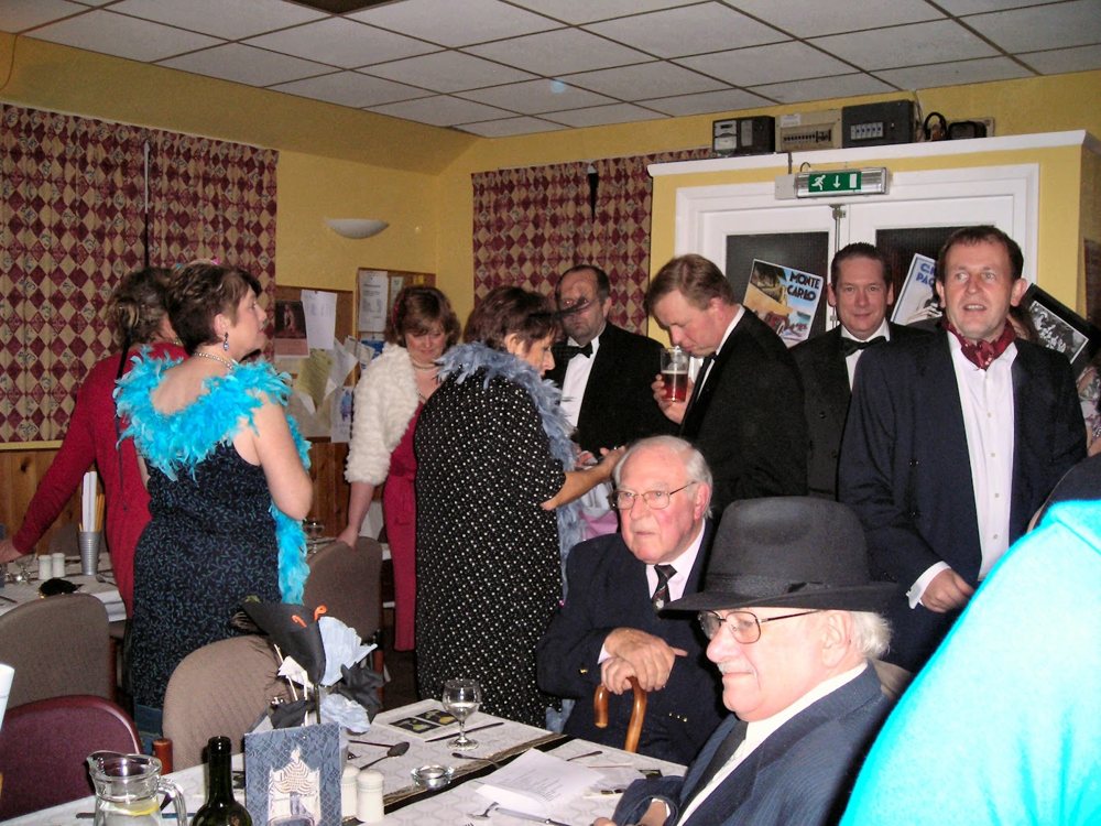 Guests in evening dress and feather boas gathered among the tables in the old hall