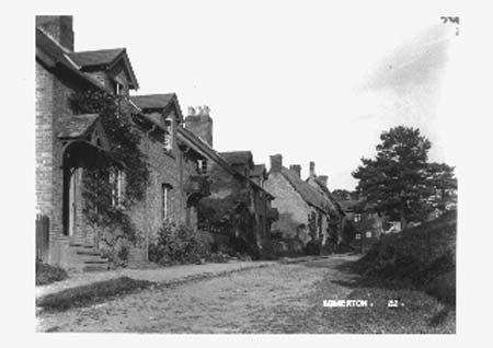 A row of brick cottages with porches beside an unmade road, on an old postcard numbered 22